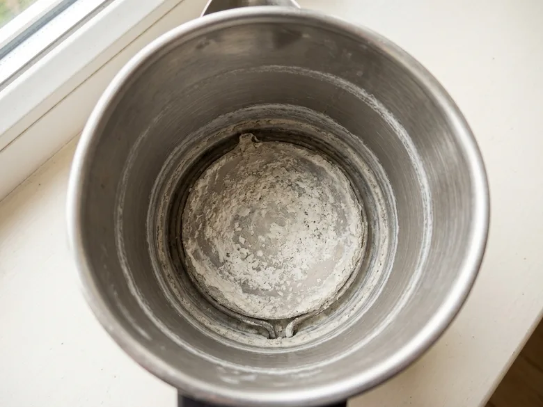 Vue plongeante dans une bouilloire ouverte : la résistance et une ligne de tartre blanche à hauteur d’eau